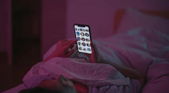 Individual scrolling on smartphone in bed highlighting Phone Addiction and late-night sleep disturbance
