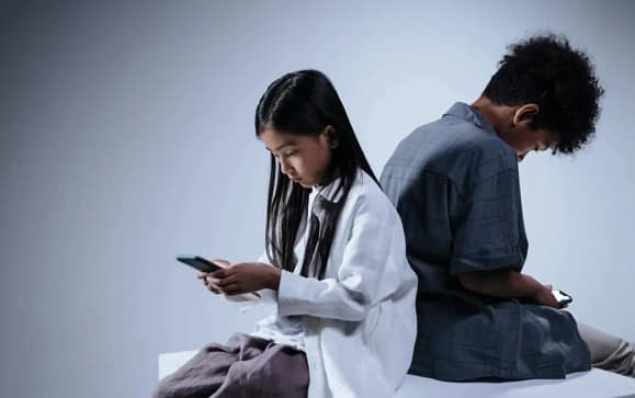 Couple sitting together but distracted by smartphones showing relationship strain caused by Phone Addiction